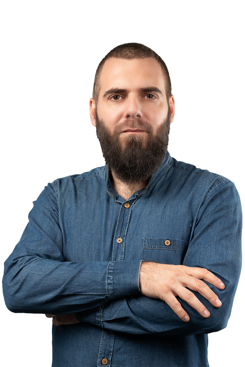 Man with a full beard wearing a blue denim shirt with folded arms, looking at the camera.