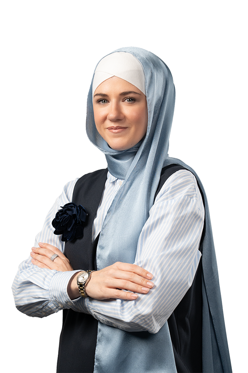 Confident woman wearing a light blue hijab, striped shirt, black vest with a black flower pin, and a wristwatch, standing with arms crossed.