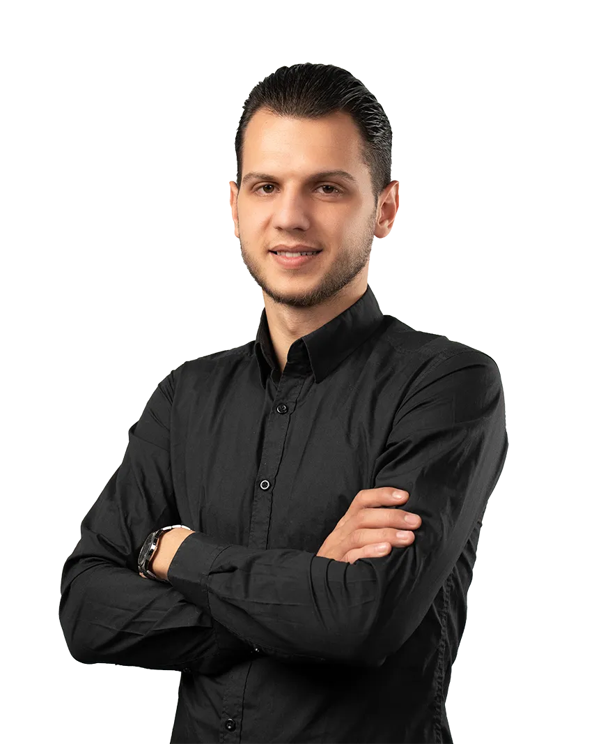 Young man with slicked-back hair wearing a black button-up shirt, standing with arms crossed and smiling.