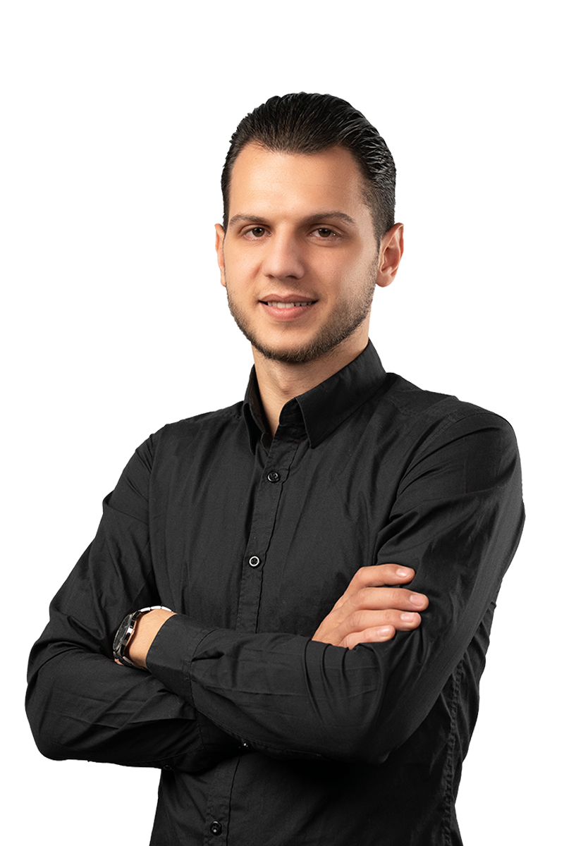Young man with neatly combed dark hair wearing a black button-up shirt, standing with arms crossed and smiling.