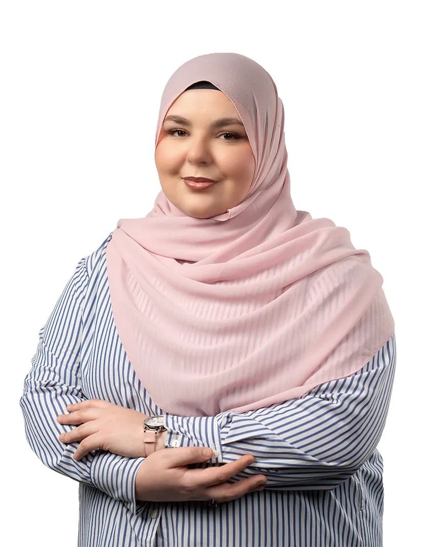 Smiling woman wearing a pink hijab and blue-and-white striped shirt with arms crossed.