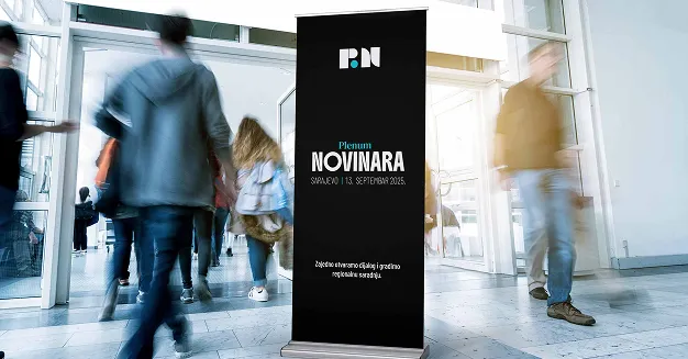 Black banner in a busy indoor hallway with people walking past, displaying text about the Plenum Novimara event happening in Sarajevo in September 2025.