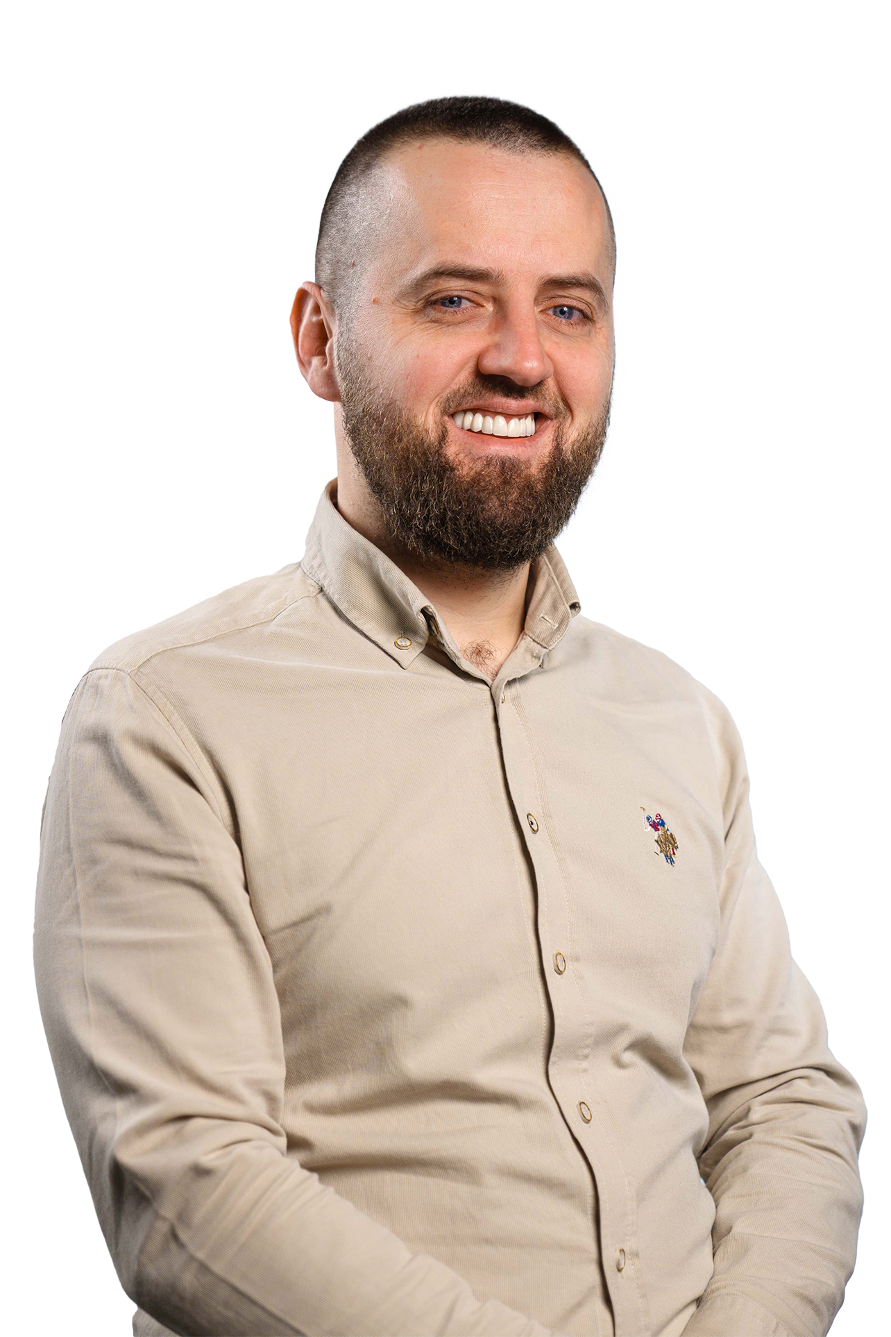 Smiling man with a beard wearing a beige button-up shirt with a small embroidered logo on the chest.