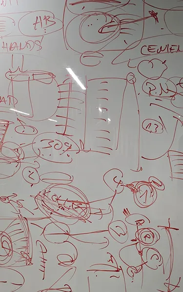 Whiteboard with red marker sketches, diagrams, and illegible handwritten notes scattered across the surface.