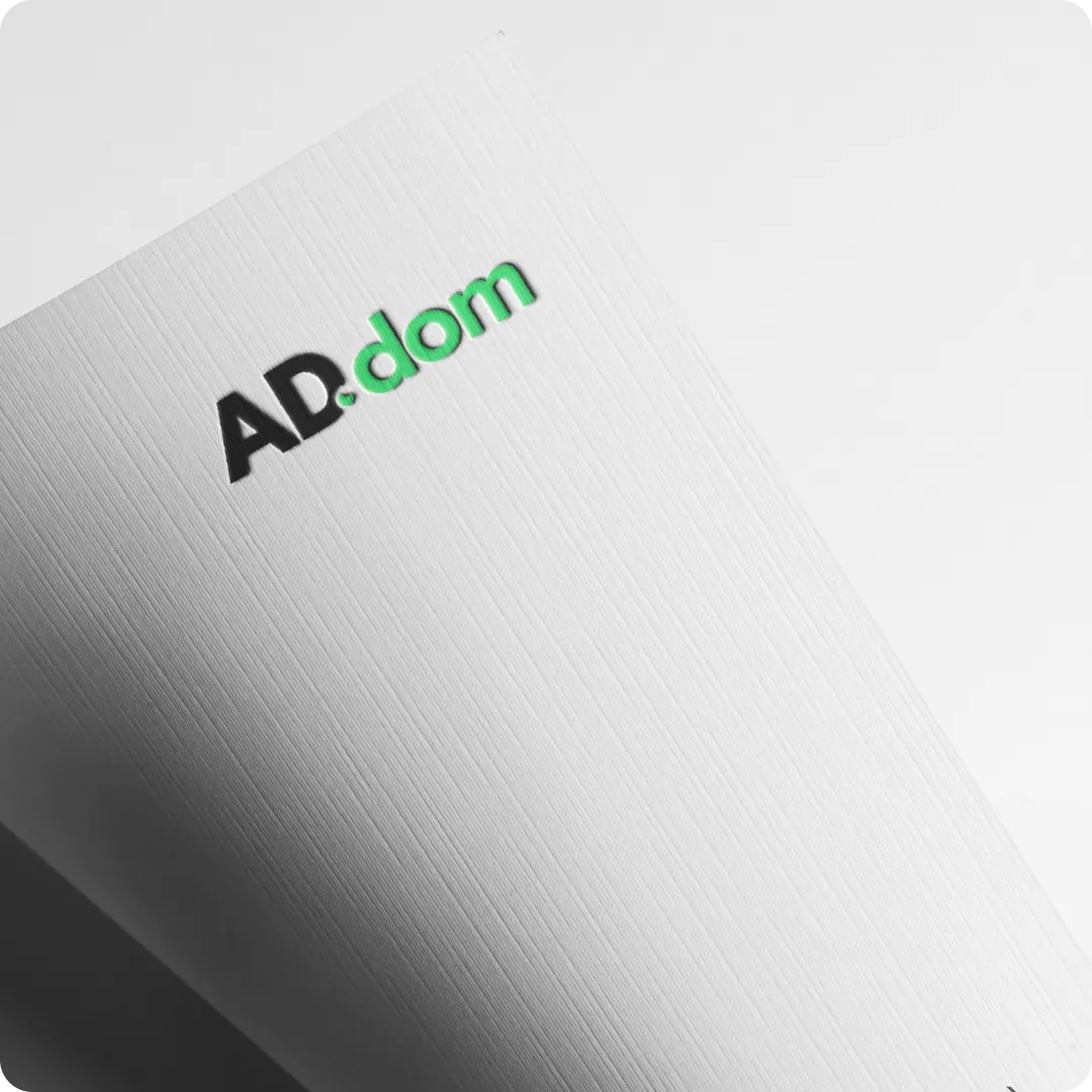 Text logo showing 'AD.dom' with 'AD' in black and '.dom' in green on textured white paper.