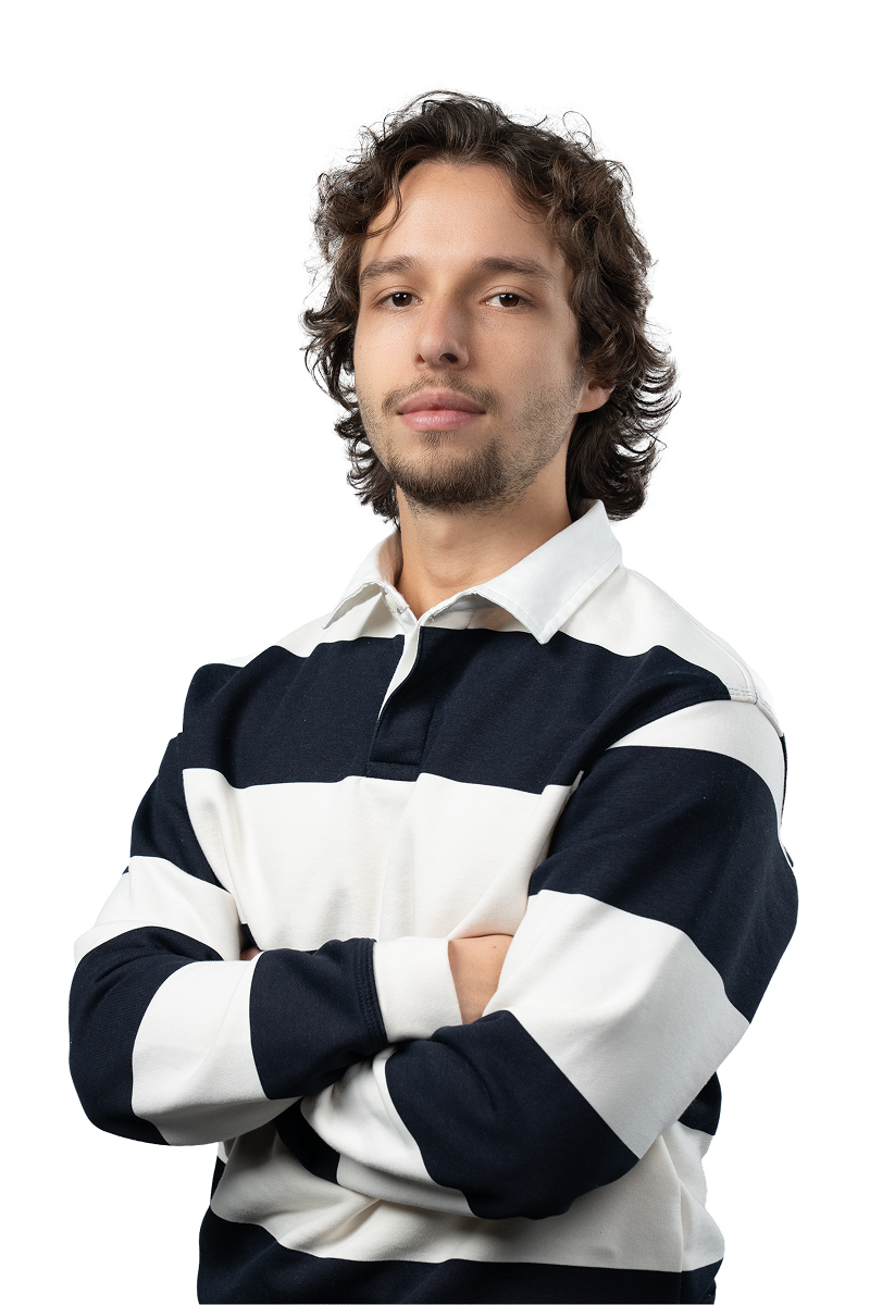 Young man with curly hair and a short beard wearing a black and white striped long-sleeve shirt standing with arms crossed.