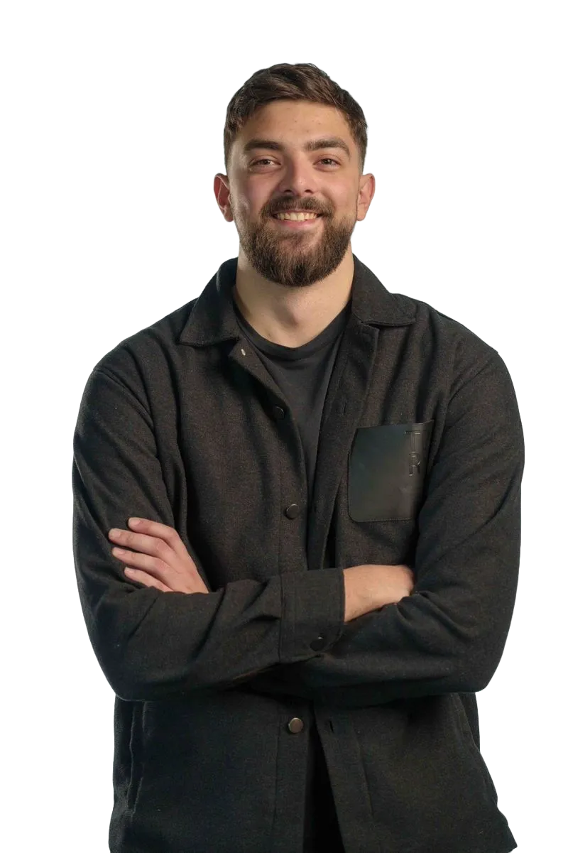 Smiling young man with dark hair and beard wearing a black jacket and black shirt, arms crossed.