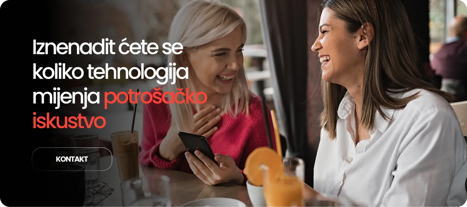 Two women smiling and conversing at a cafe table with drinks, one holding a smartphone.