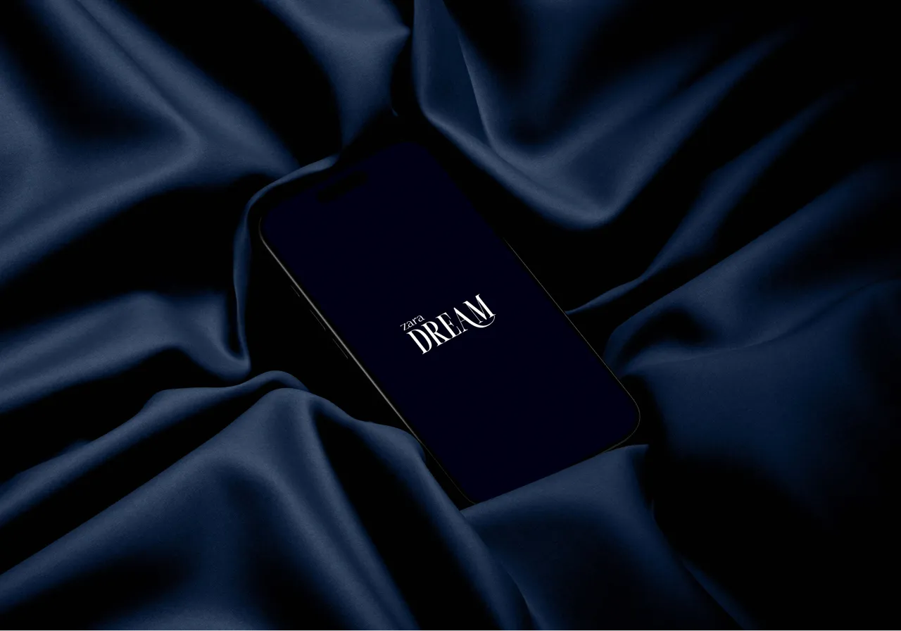 Smartphone lying on dark blue silky fabric with 'zara DREAM' text on the screen.